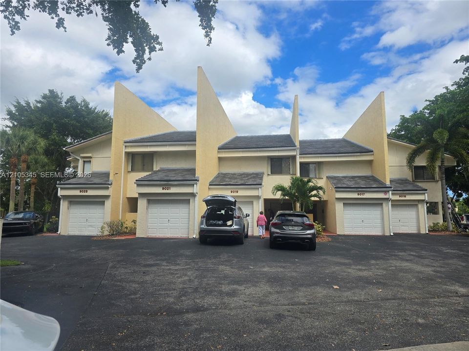 Multi-unit residential exterior featuring peaked architectural rooflines, smooth stucco facade, and individual garage access