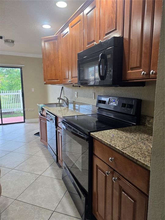 Kitchen featuring stained wood cabinetry, stone-finish countertops, black appliance suite, and tile flooring