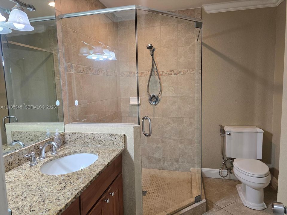 Vanity with stone countertop and undermount sink, glass-enclosed shower featuring tiled surround and handheld fixture, and neutral tile flooring