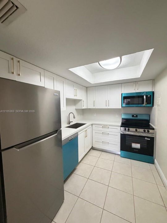 Full kitchen featuring white cabinetry, stainless steel refrigerator, built-in microwave, gas range, and white tiled flooring