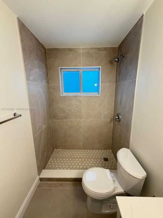 Tiled shower enclosure featuring a window, mosaic tile shower pan, and a chrome shower head