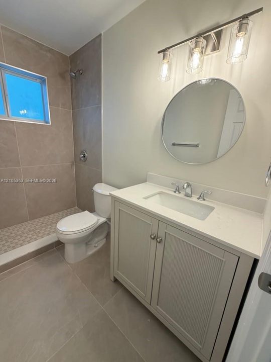 Walk-in shower with tiled walls and floor, vanity with integrated sink, contemporary wall-mounted lighting, and a circular mirror
