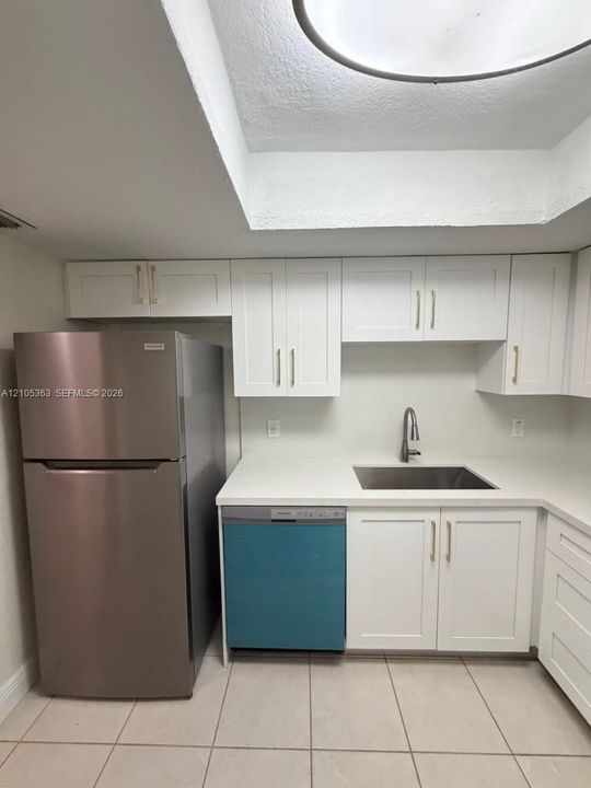 White shaker cabinetry with gold-tone hardware, stainless steel sink with gooseneck faucet, light-toned countertops, and tiled flooring