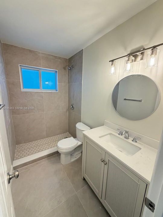 Tile flooring with a walk-in shower, a single vanity with an integrated sink, a quartz countertop, and a circular mirror