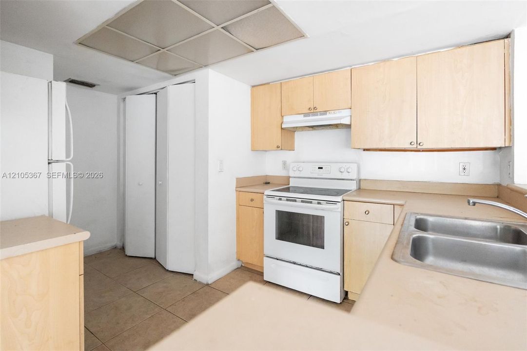 Kitchen featuring light-finish cabinetry, solid-surface countertops, dual-basin stainless steel sink, integrated range, and ceramic tile flooring
