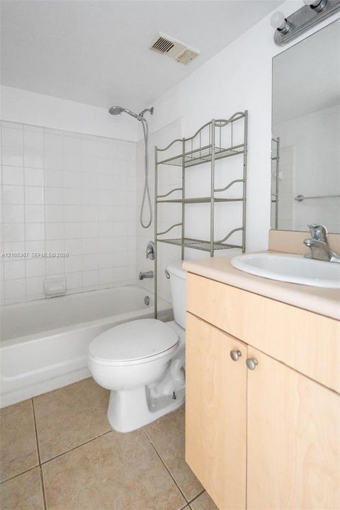 Bathroom featuring a shower and tub combination with wall-surround tile, vanity with a light-wood finish, solid-surface countertop with an integrated basin, and neutral floor tile