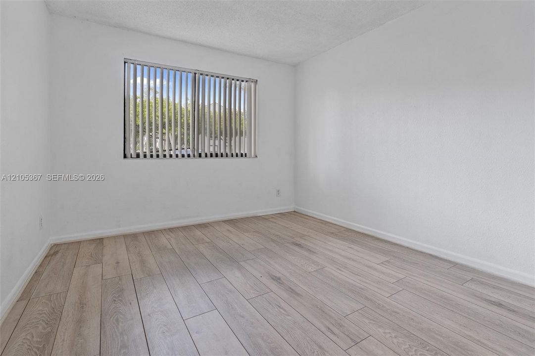 Interior space featuring neutral wall tones, wood-finish flooring, and a window with vertical blinds