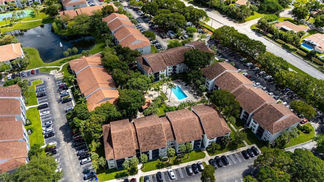Aerial view of a residential complex featuring tile roofing, an outdoor swimming pool, mature landscaping, and an on-site pond with a fountain