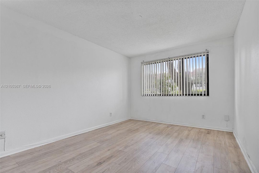 Interior space featuring light-toned wood-finish flooring, white walls, and a window with vertical blinds