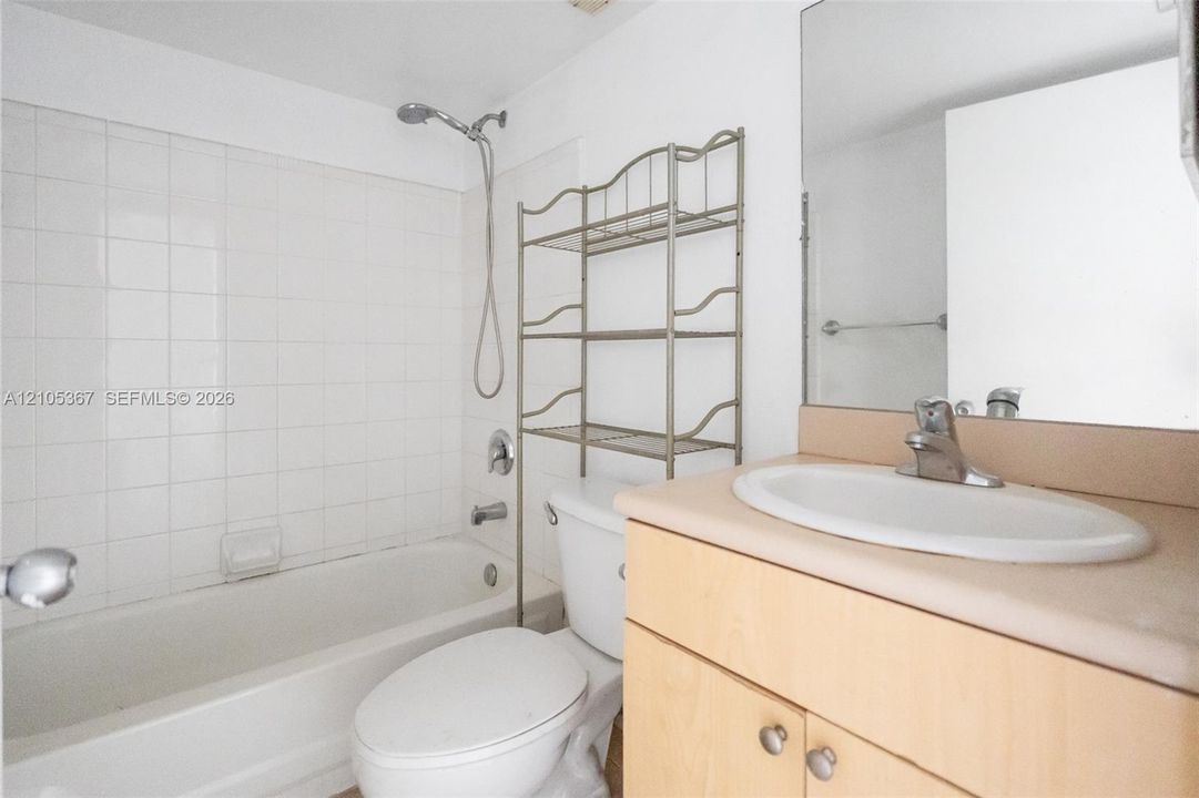 Bathroom featuring a bathtub with a tiled surround, a showerhead on a flexible hose, a wood-finish vanity with a molded countertop sink, and a wall-mounted mirror