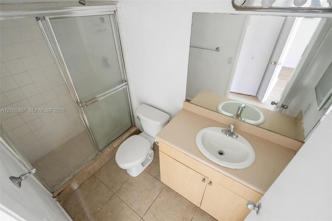Bathroom featuring a vanity with an integrated basin, a large wall-mounted mirror, ceramic tile flooring, and a glass-enclosed shower stall with tiled surround