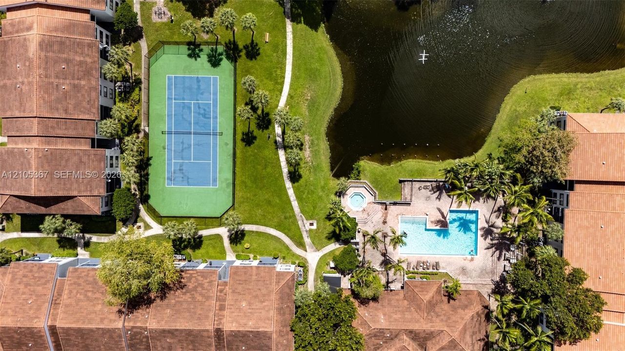 Aerial perspective of a multi-unit complex featuring a fenced tennis court, swimming pool, spa, and a natural pond