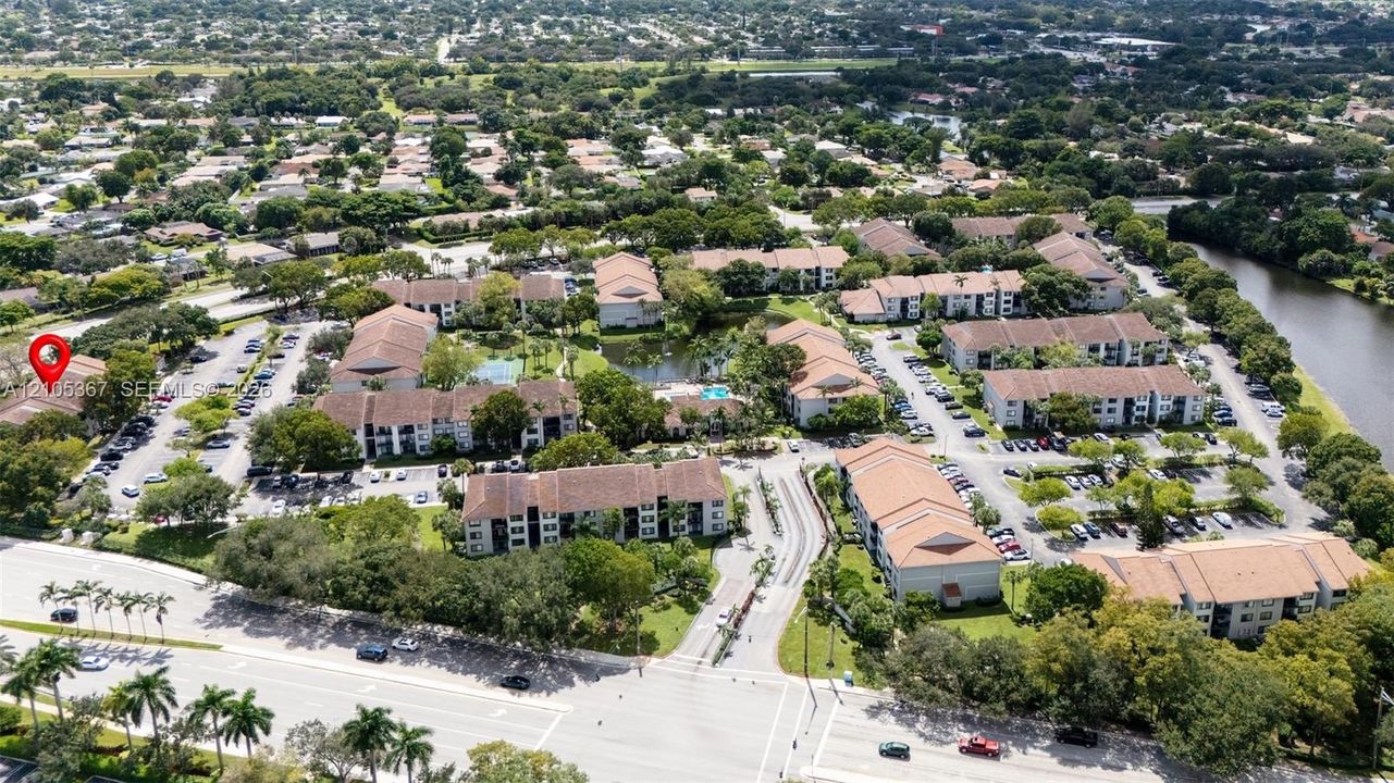 Aerial perspective of a multi-building residential community featuring tile roofs, paved parking lots, landscaped grounds, and proximity to a canal