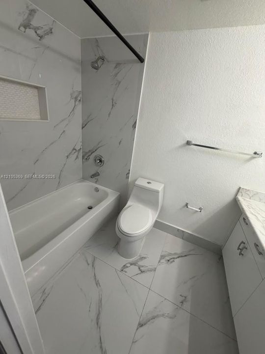 Contemporary bathroom featuring large format tile flooring, a built-in shower niche with mosaic tile, a white bathtub, and a modern toilet