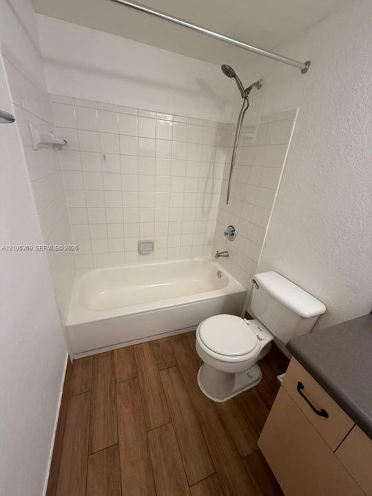 Bathroom featuring wood-finish flooring, a built-in bathtub, white subway tile surround, and a vanity with a dark countertop