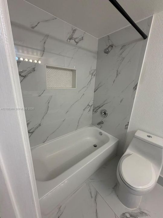 Full bath featuring a white bathtub, toilet, and white tile with gray veining