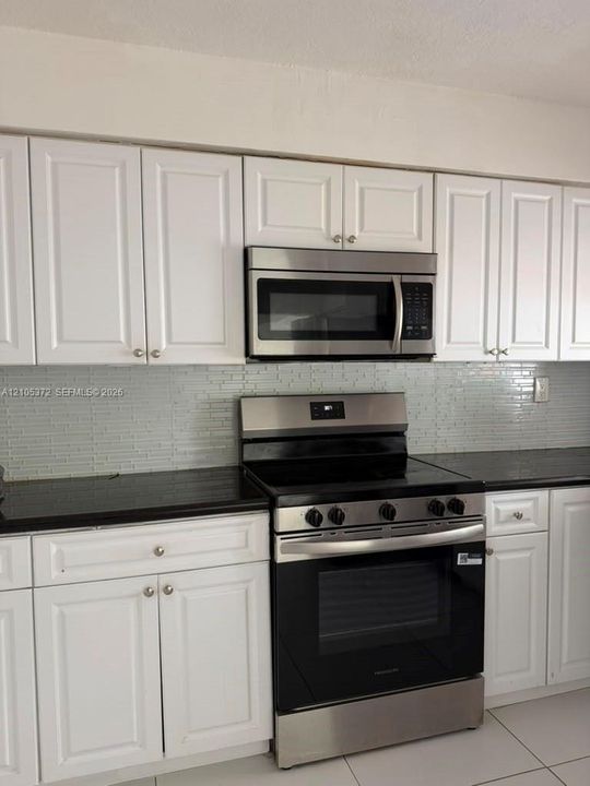 White shaker-style cabinetry, black countertops, stainless steel range, coordinating stainless steel microwave, and a tiled backsplash