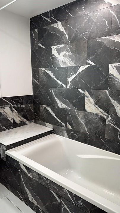 Bathtub with black marble-look tile surround and a contrasting white tub basin