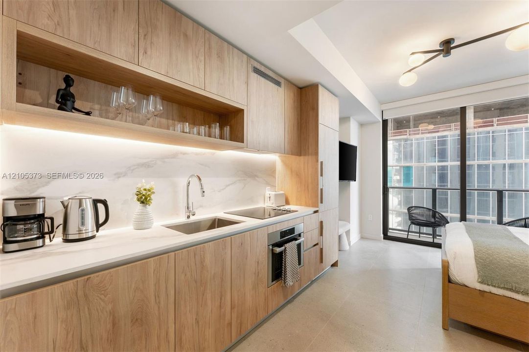 Kitchenette featuring integrated cabinetry, white countertop, stone-finish backsplash, and under-cabinet lighting