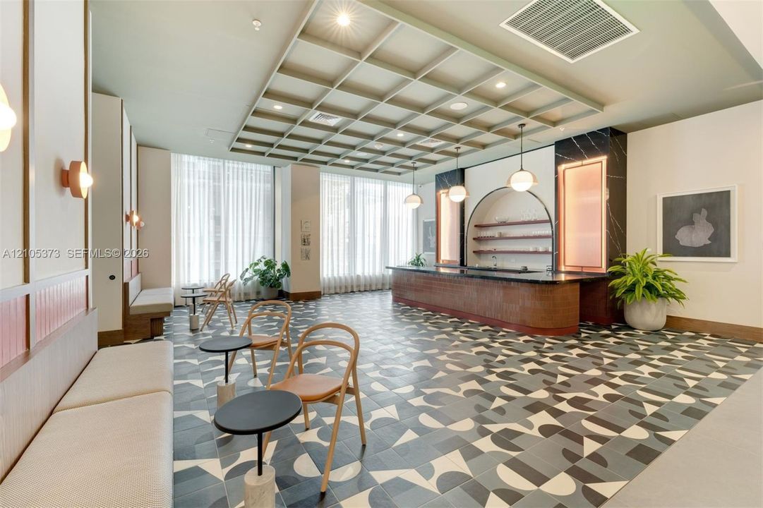 Patterned floor tiling, coffered ceiling with recessed lighting, built-in bench seating, wood-paneled counter with integrated shelving, and full-height windows with sheer drapery