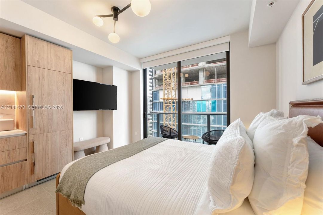 Built-in wood-finish cabinetry, integrated wall-mounted television, full-height window, balcony access, and hard surface flooring