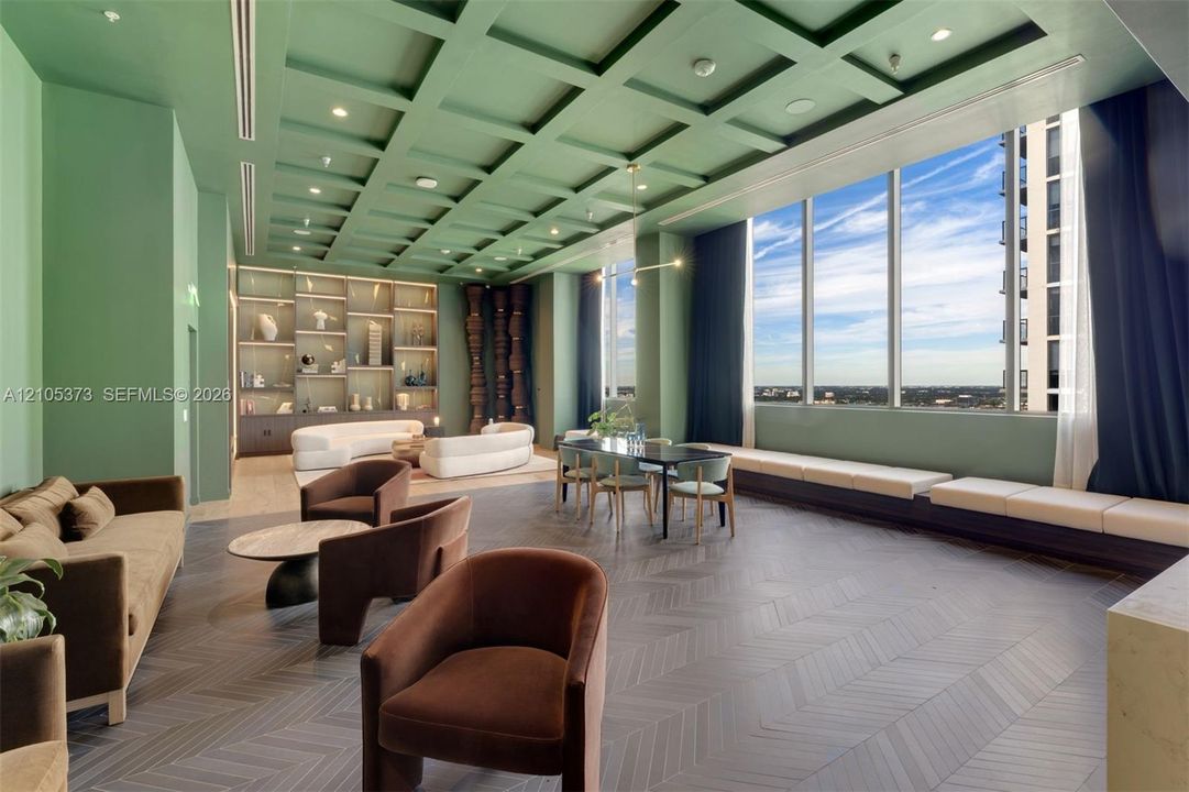 Spacious lounge area featuring a coffered ceiling, floor-to-ceiling windows, built-in shelving with integrated lighting, and herringbone pattern flooring
