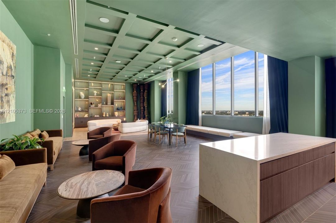 Expansive common area featuring a coffered ceiling, floor-to-ceiling windows, built-in shelving, a large central island with a solid surface countertop, and wood-finish flooring