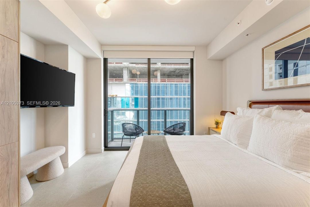 Floor-to-ceiling glass door leading to a private balcony, featuring a wall-mounted television, recessed lighting, and a contemporary ceiling fixture