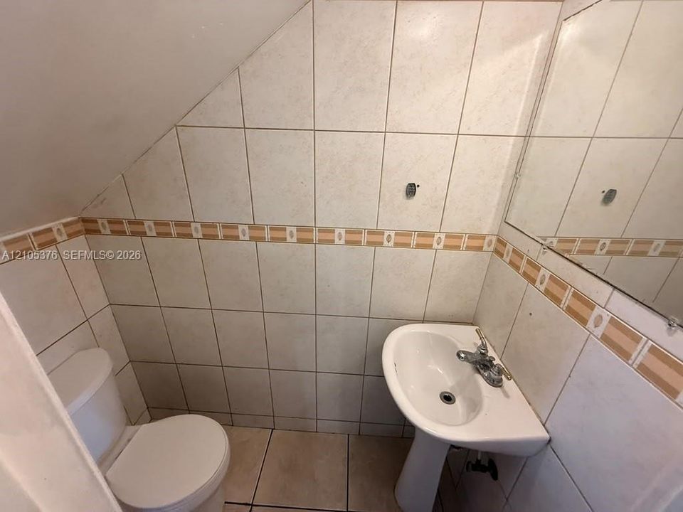 Pedestal sink, wall-mounted mirror, and tiled walls with a decorative border