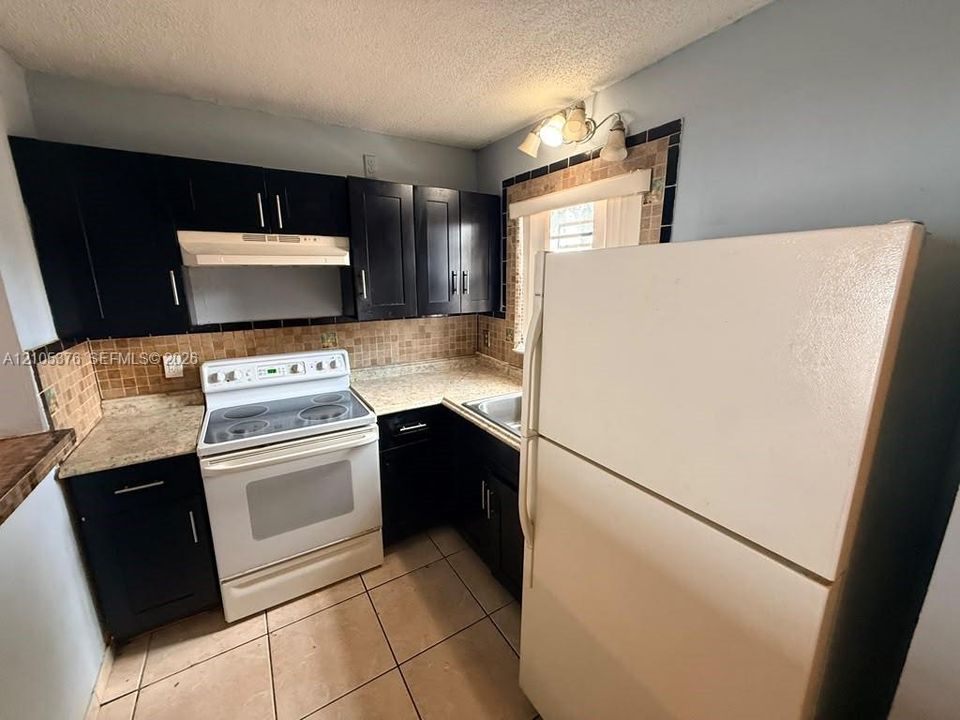 Kitchen with dark cabinetry, light-colored countertops, tile backsplash, and tile flooring