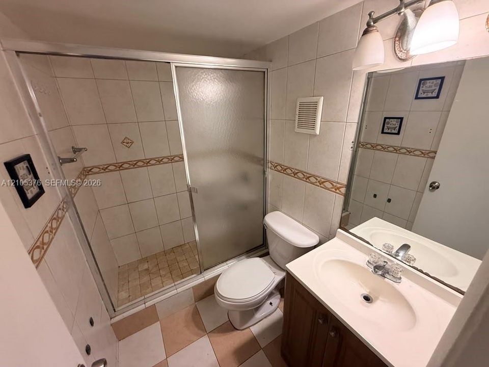Tiled shower stall with a sliding glass door, white vanity with an integrated sink, and a wall-mounted mirror