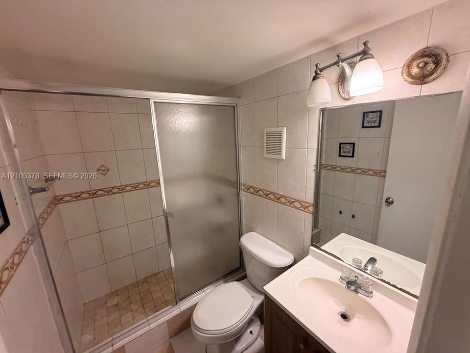 Bathroom featuring a tiled shower with a sliding glass enclosure, white toilet, and a vanity with an integrated sink