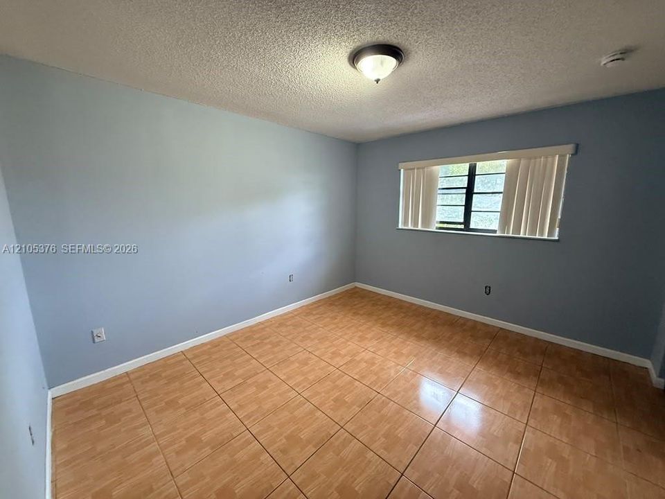 Tile flooring, light blue painted walls, window with horizontal blinds, overhead light fixture, textured ceiling