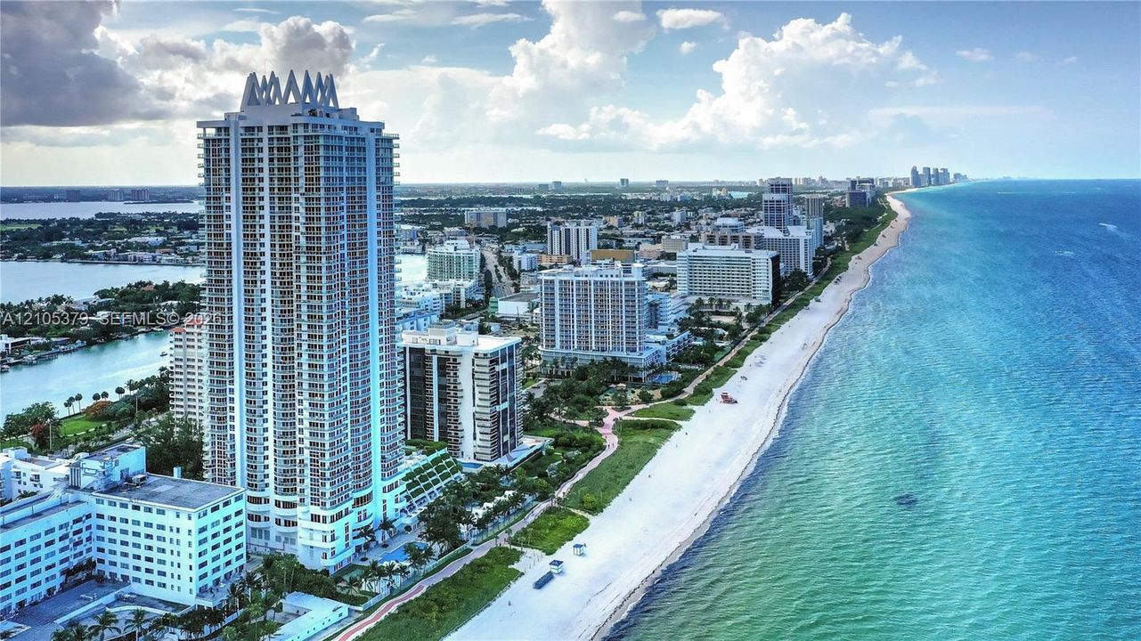 Coastal property featuring a high-rise building with multiple balconies, a white sand beach, and clear blue ocean waters