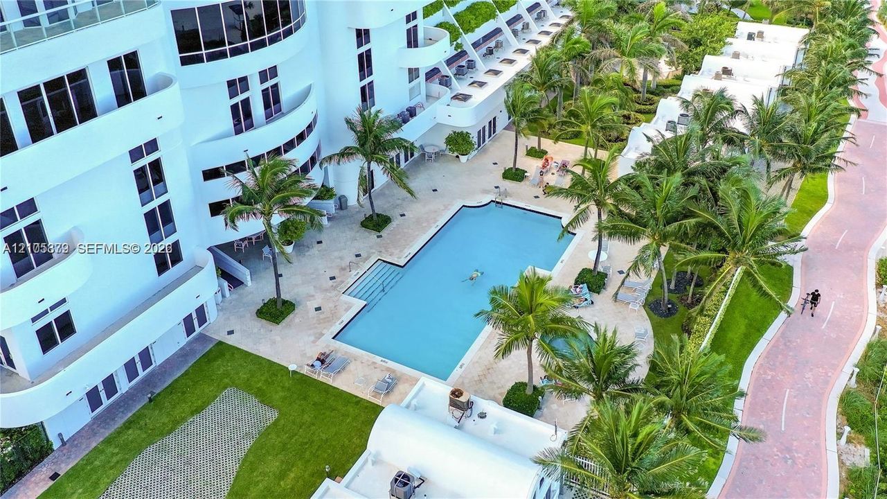 Outdoor swimming pool and spa area featuring stone-paver decking, mature palm trees, landscaped green space, and brick-paved walking paths