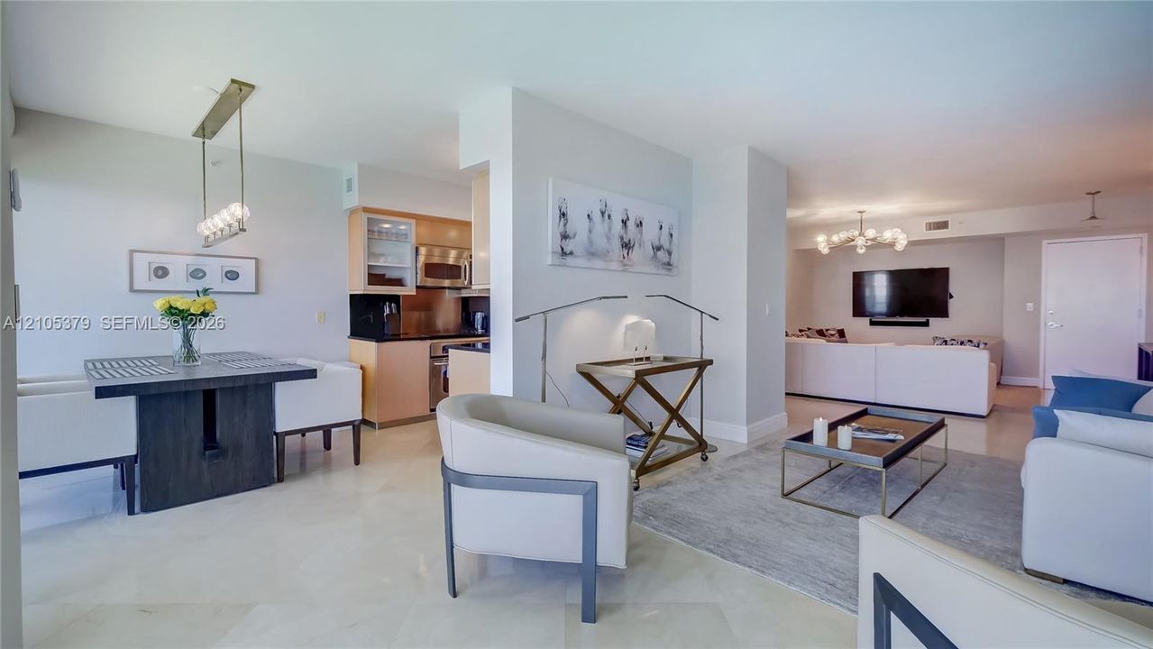 Open-concept living area with light-toned flooring, a dining area featuring a linear pendant light fixture, and a kitchen with wood-finish cabinetry and stainless steel appliances