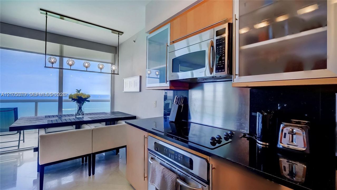 Modern kitchen featuring stainless steel appliances, black countertops, and light wood-finish cabinetry