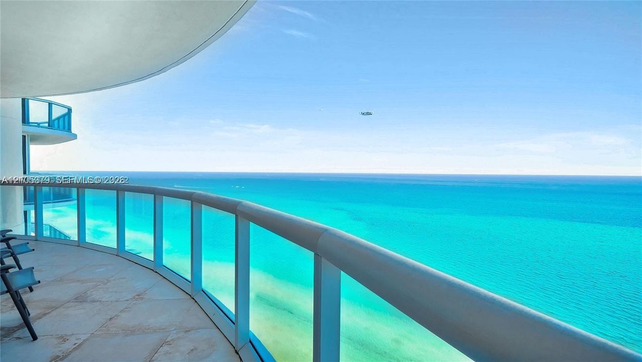 Curved balcony with glass and metal railing, offering expansive ocean scenery