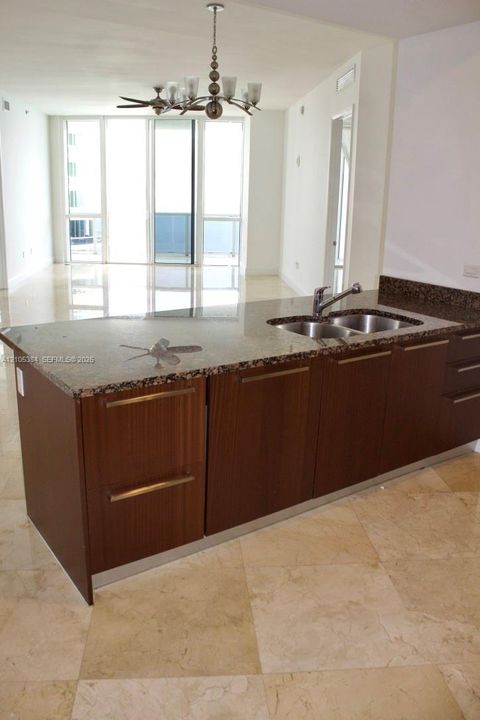 Kitchen island with stone countertop, stainless steel double basin sink, and wood-finish cabinetry