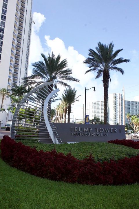 Landscaped entrance featuring a prominent monument sign, manicured shrubs, and mature palm trees