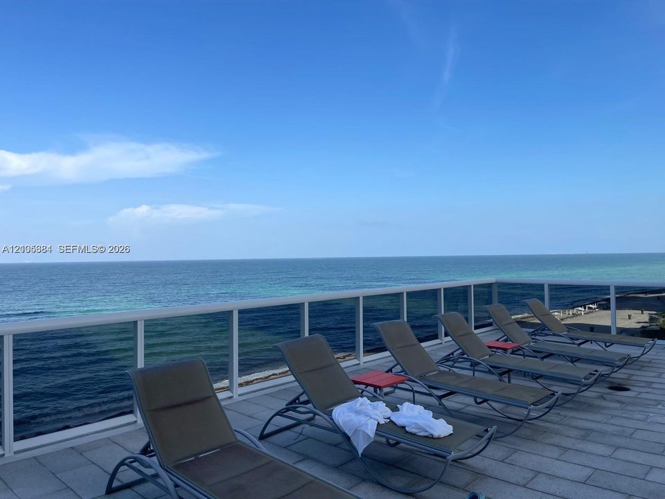 Oceanfront deck with multiple lounge chairs, composite decking, and metal railings overlooking pristine waters and clear blue skies