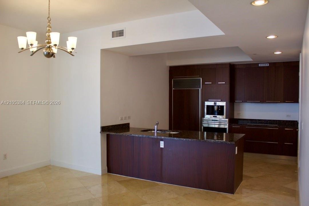 Kitchen featuring dark wood-finish cabinetry, integrated stainless steel appliances, a center island with a dark countertop, and recessed lighting