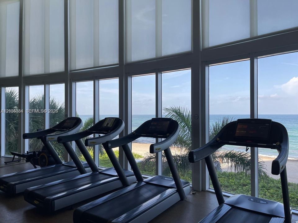 Floor-to-ceiling windows with roller shades, a scenic ocean backdrop, and integrated fitness equipment