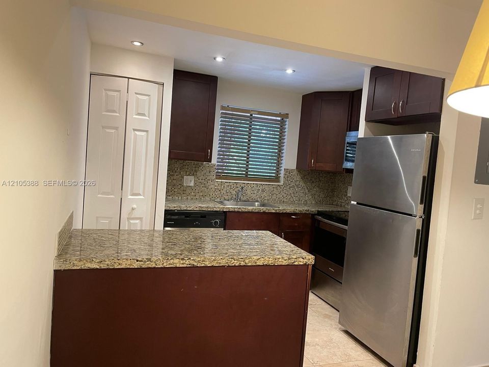 Kitchen featuring dark wood-finish cabinetry, granite countertops, a matching granite backsplash, and stainless steel appliances