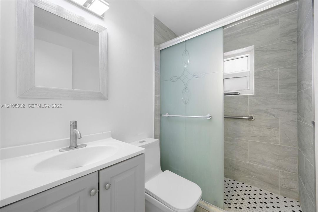 Modern vanity with undermount sink, a framed mirror, and a frosted glass shower door with patterned detail