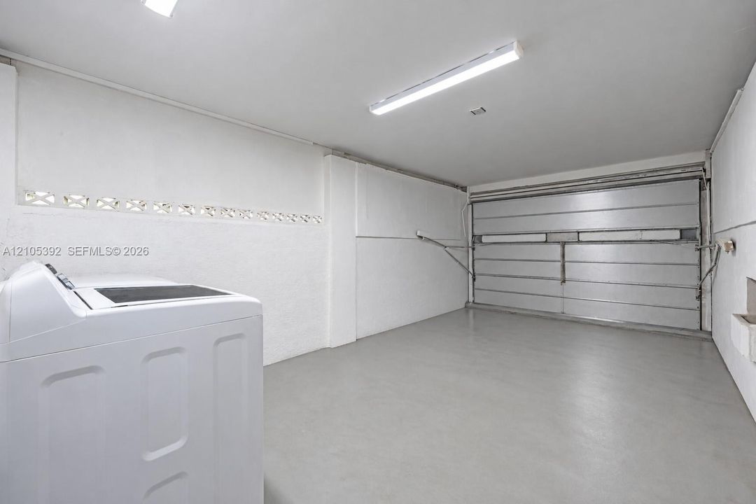 White walls, concrete flooring, fluorescent lighting, and a metal roll-up door