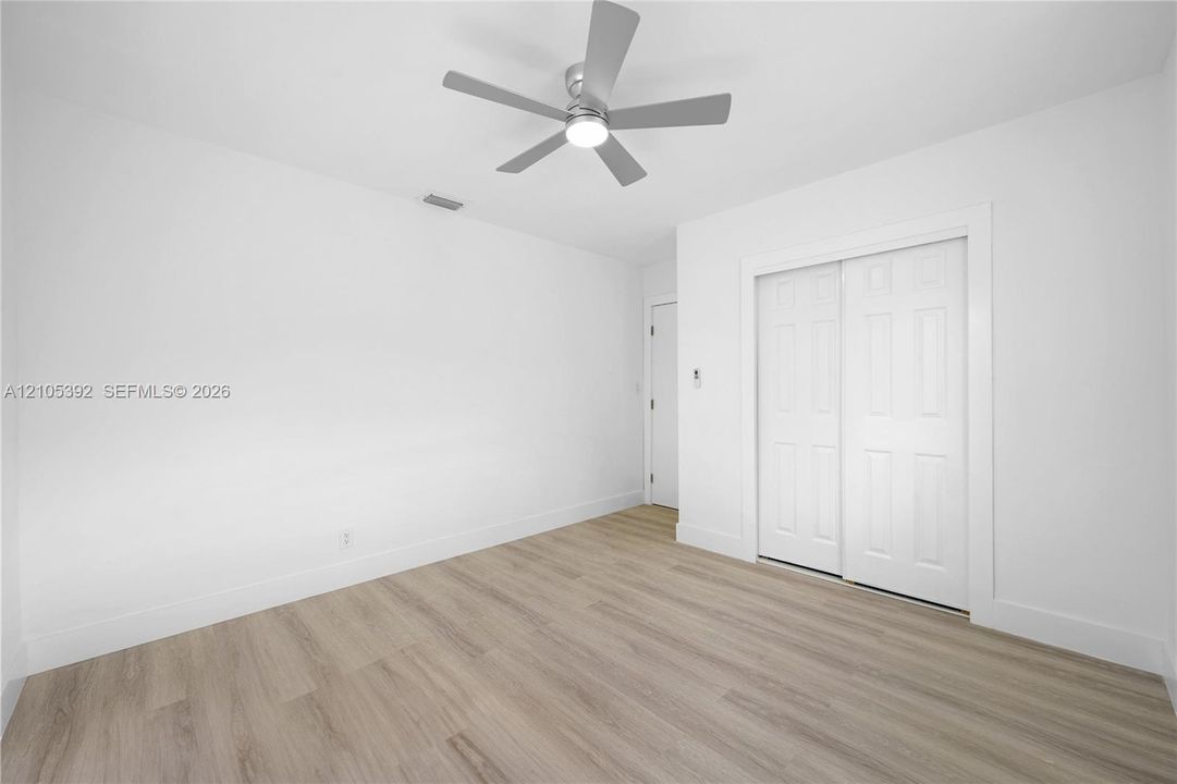 Light-toned wood-finish flooring, white walls, and a contemporary ceiling fan with integrated lighting