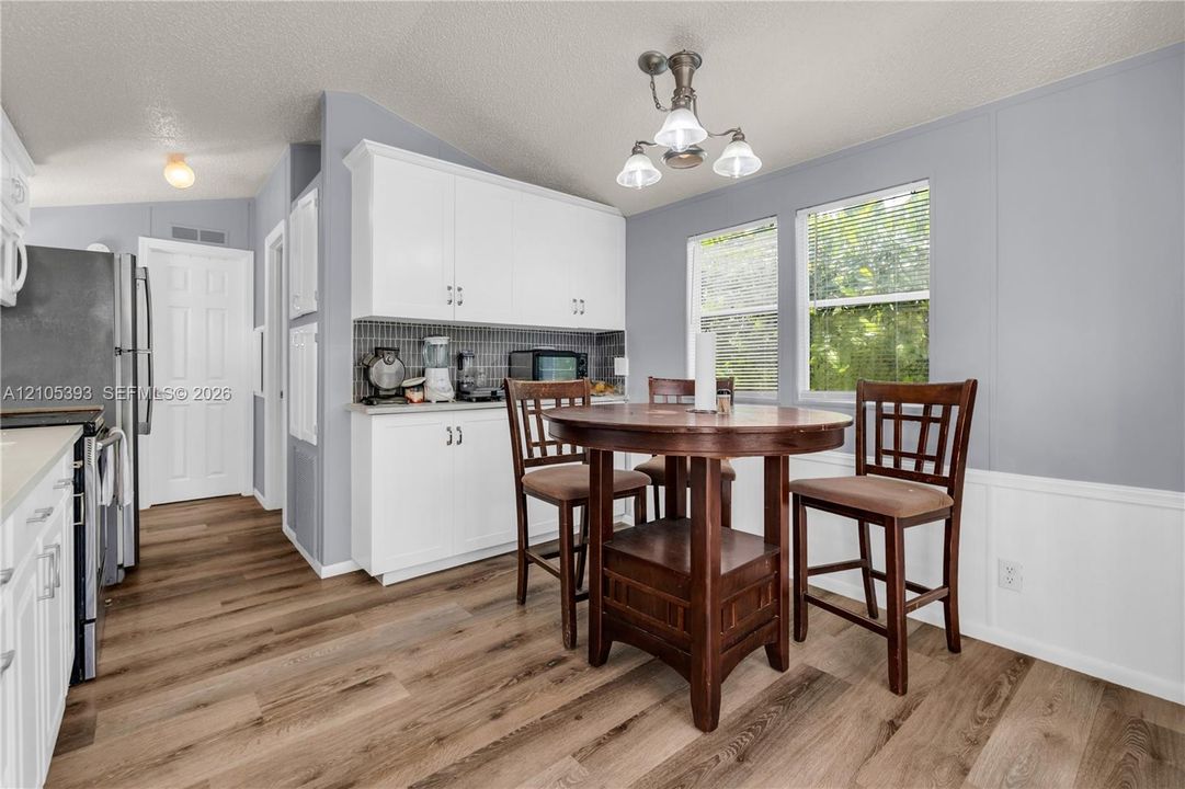 Kitchen featuring white shaker-style cabinetry, a tiled backsplash, wood-finish flooring, and a multi-light metal chandelier