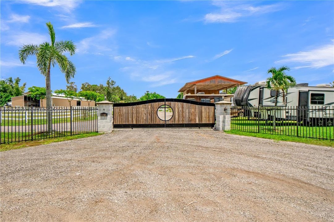 Gated entry featuring a custom wood-paneled sliding gate with circular detailing, mounted between masonry columns and connected to black metal perimeter fencing