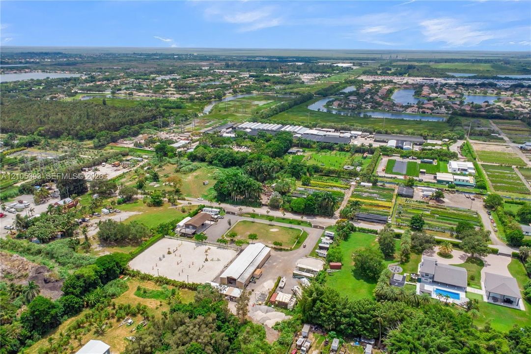 Aerial perspective of expansive acreage featuring an outdoor riding arena, a multi-stall stable structure, open pasture space, and a swimming pool
